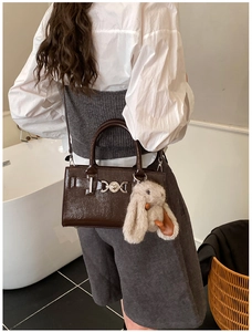Détail d'un sac bandoulière en cuir marron brillant avec charm lapin en peluche sur un mannequin