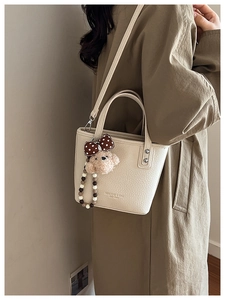 Chic beige bucket bag detail featuring a cute teddy bear charm and branded texture