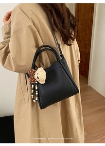 Detail of black litchi grain bucket bag with teddy bear charm and pearl chain decoration