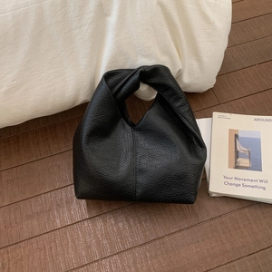Détail d'un sac hobo noir minimaliste avec poignée nouée sur le sol à côté d'un magazine