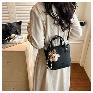 Detail of black textured bucket bag with a cute plush bear charm and long shoulder strap