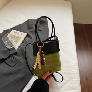 Detail of a mini bucket bag with green suede, black leather, and wood bead tassel charm