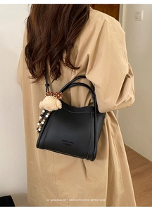 Detail of a black leather bucket bag with brand logo and a cute teddy bear charm accessory