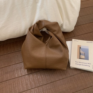 Détail d'un sac en cuir marron foncé avec une poignée nouée au design unique et épuré