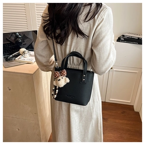 Detail of black pebbled leather bucket bag with cute teddy bear charm accessory