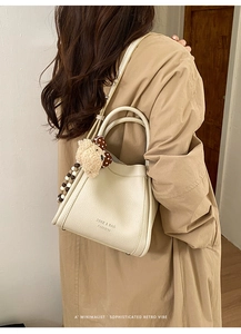 Detail of beige lychee grain leather bucket bag with cute plush bear charm and brand logo