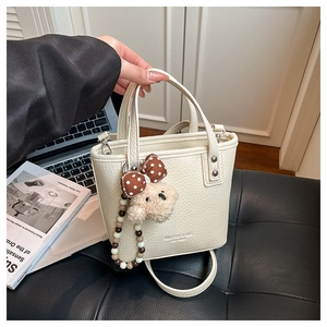 Detail of cream bucket bag with pebble leather texture and cute plush bear charm