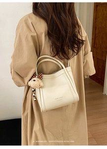 Creamy white litchi leather bucket bag shown on model with cute plush bear charm decoration