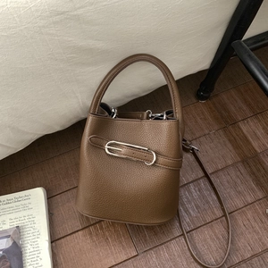 Detailaufnahme einer dunkelbraunen Eimer-Tasche aus Leder mit silbernen Schnallen auf Holz