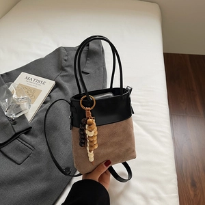 Detail of two-tone bucket bag with quilted suede panel and wooden bead charm accessory