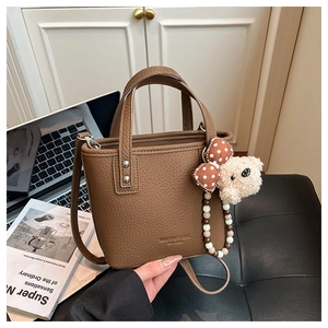 Close-up of brown pebbled leather bucket bag with cute bear charm and bead tassel