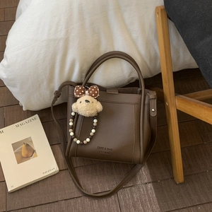 Detail of dark brown bucket bag with lychee texture and cute plush bear charm