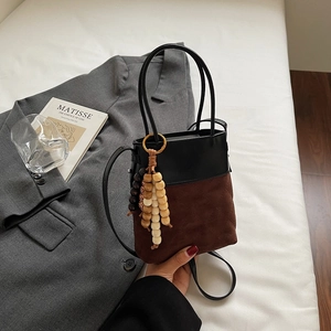 Detail of color-block bucket bag with quilted suede, leather top, and wooden bead charm