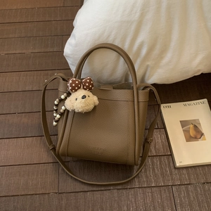 Detailed view of dark brown litchi pattern leather bucket bag with cute plush bear charm