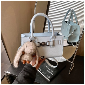 Détail du sac carré bleu clair avec fermoir cœur, breloque lapin et reflet dans le miroir