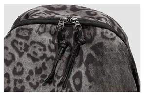 Detailed macro view of the double zipper and red embroidered logo on leopard print backpack