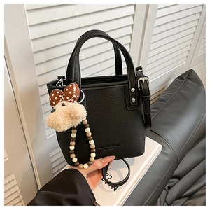 Close-up of black lychee grain bucket bag with dual handles and plush dog charm accessory