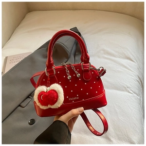 Detail of red polka dot shell bag with white plush apple charm and long strap