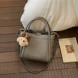 Detail of grey lychee leather bucket bag with plush dog charm and cylinder handle