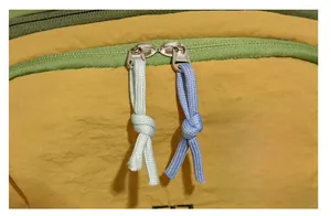 Dettaglio di cerniere metalliche a due vie con tiranti in corda intrecciata su zaino giallo