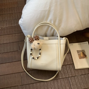 Detail of off-white lychee leather bucket bag with cute bear charm and logo print