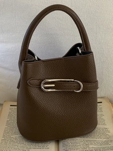 Dunkelbraune Eimer-Tasche aus Kieselleder mit Silberschnalle auf Vintage-Buchhintergrund