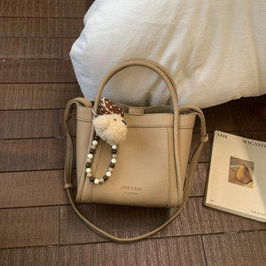 Detail of khaki litchi leather bucket bag with bear charm and beaded accessories