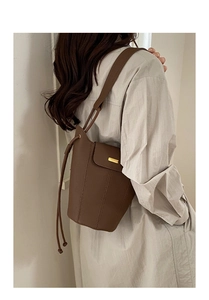 Détail d'un sac seau en cuir grainé marron foncé avec fermoir doré et pampille latérale