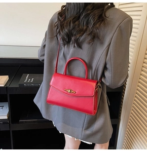 Detail of red leather crossbody bag with gold metal buckle on dark grey blazer