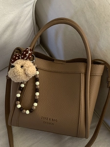 Brown litchi leather bucket bag with plush dog charm and adjustable shoulder strap