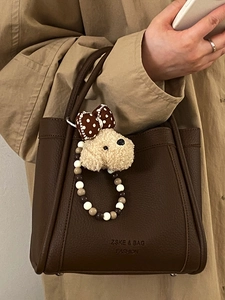 Brown leather bucket bag with poodle charm and beaded handle shown on classic khaki trench coat