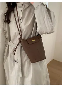 Sac seau en cuir grainé marron foncé avec plaque dorée porté par un mannequin