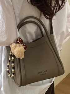 Chic taupe bucket bag with lychee texture and cute bear charm shown on model