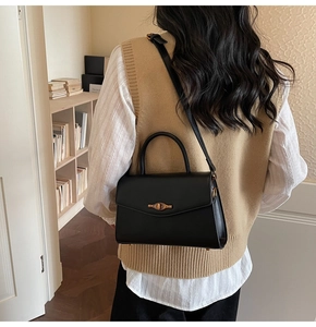 Detail of a chic black square bag with a vintage gold twist lock on textured leather