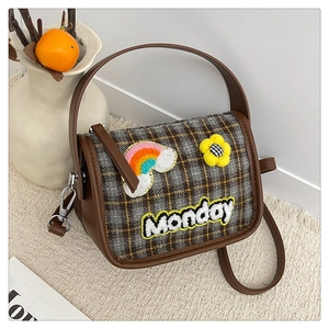 Detail der karierten Umhängetasche mit Monday-Stickerei und süßen Blumenanhängern
