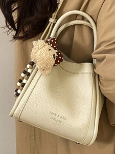 Chic beige lychee leather bucket bag with plush bear charm and crossbody strap