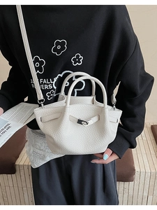Détail du sac seau crème avec texture litchi et fermoir argenté sur une tenue noire