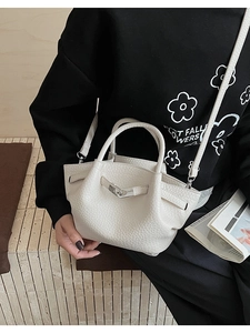 Détail de la texture en cuir litchi blanc crème et de la boucle argentée du sac seau