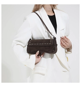 Close-up of brown suede underarm bag featuring silver rivets on a white blazer