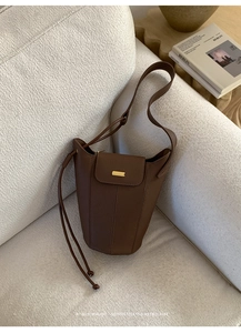 Détail du sac seau en cuir marron foncé avec boucle dorée et coutures verticales