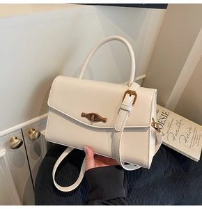 Detail of white structured handbag with vintage gold eye-shaped twist lock and top handle