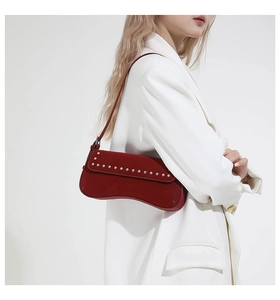 Detail of dark red suede baguette bag featuring silver rivet trim and a curved base design