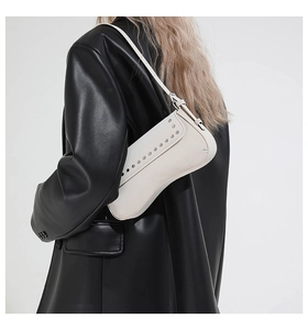 Detail view of cream leather underarm bag with silver rivet studs on curved flap cover