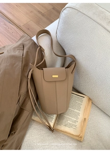Détail du sac seau en cuir kaki avec fermoir doré dans un décor au style minimaliste