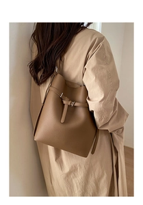 Close-up of pebble leather texture and metal buckle on dark camel bucket shoulder bag