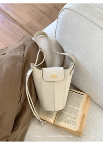 Détail d'un sac seau en cuir beige avec finitions dorées posé sur des livres vintage