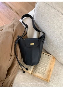 Détail du sac seau rétro en cuir noir à motif litchi sur un canapé avec livre de décoration