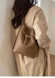Detailed texture of brown litchi grain leather bucket bag worn with a beige coat