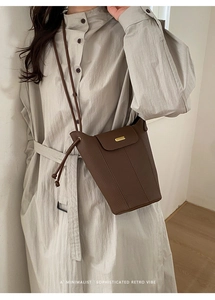 Détail du sac seau en cuir marron foncé avec boucle dorée sur mannequin en trench