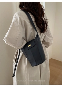 Détail du sac seau noir en cuir grainé avec une boucle dorée et un cordon décoratif
